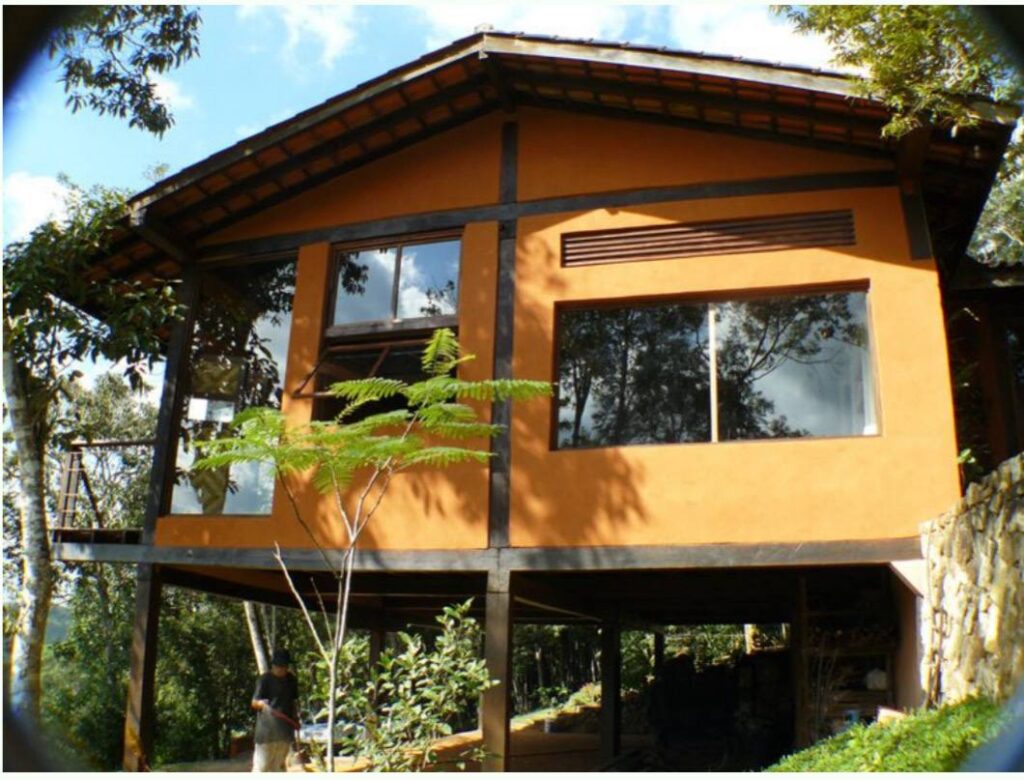 Casa moderna com fachada pintada em tons terrosos, utilizando tintas ecológicas à base de insumos naturais e não tóxicos, cercada por jardim.