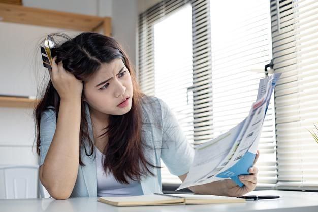 Mulher estressada diante do notebook e contas em atraso ilustrando dívidas e score baixo