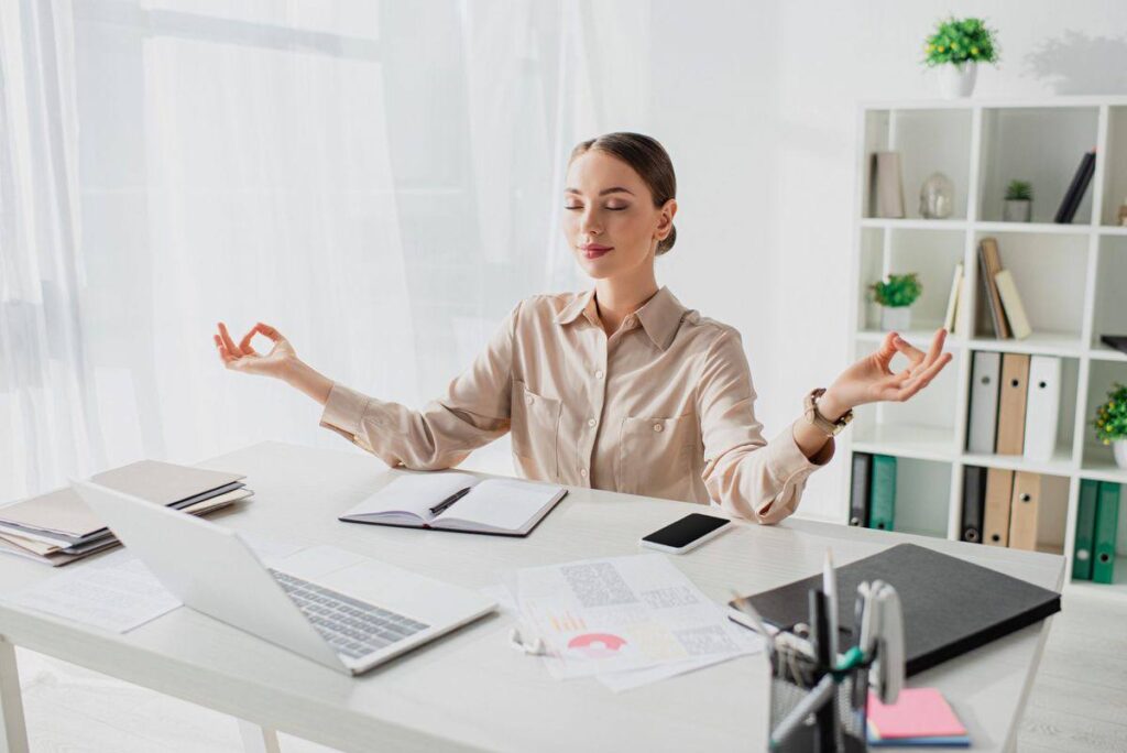 Mulher serena meditando no ambiente de trabalho, representando equilíbrio emocional e mentalidade de cura em ambientes tóxicos.