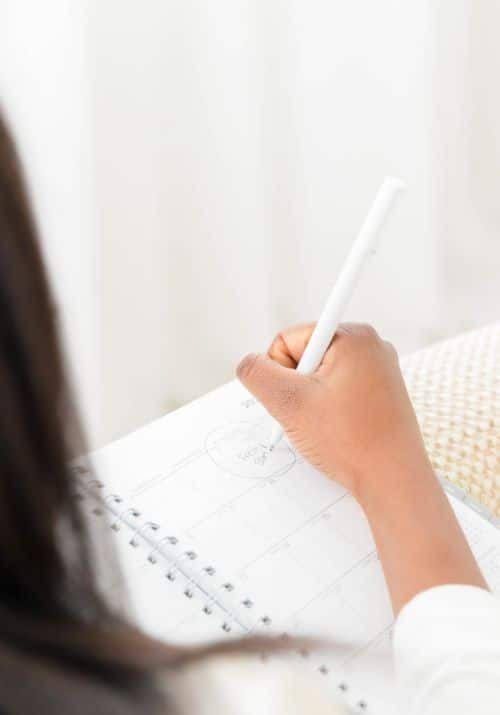 Mulher moderna escrevendo em seu planner e analisando prioridades, representando equilíbrio e foco em meio a uma rotina cheia de urgências.