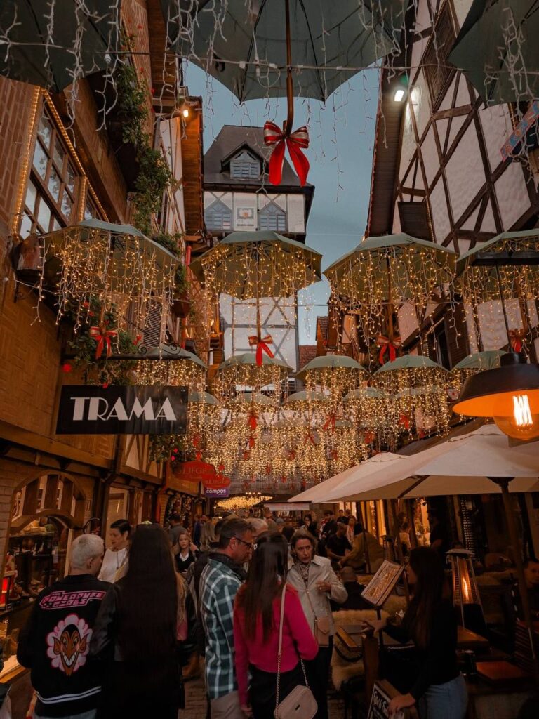 Rua decorada com luzes de Natal em Campos do Jordão, com guarda-chuvas iluminados e visitantes caminhando, representando o clima festivo das cidades natalinas do Brasil
