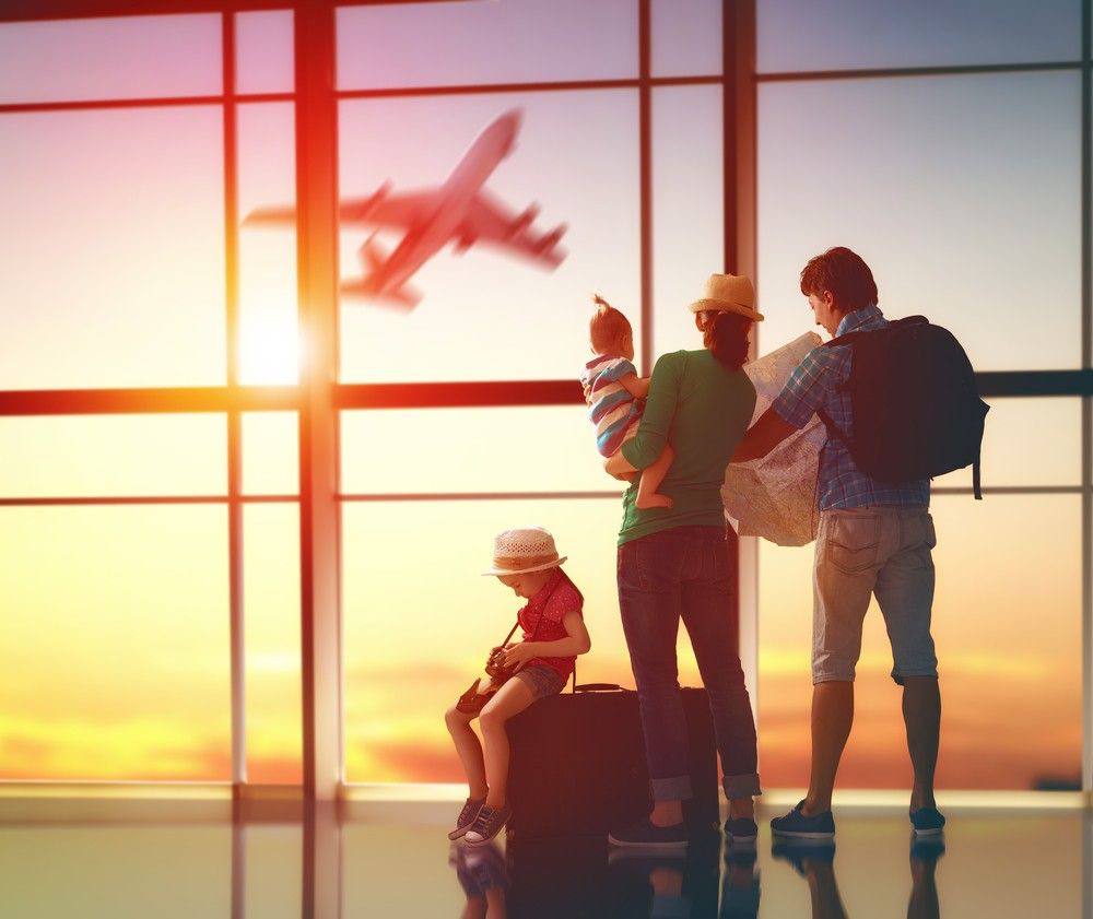 Família com crianças no aeroporto observando um avião decolar ao pôr do sol, simbolizando planejamento para uma viagem econômica