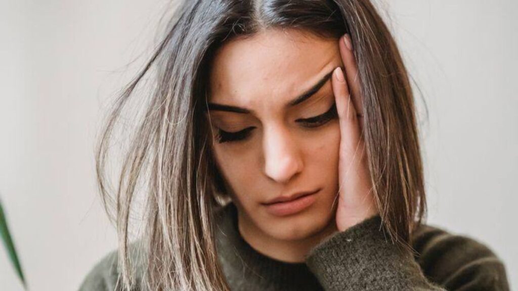 Mulher preocupada olhando o celular, refletindo sobre autossabotagem financeira e suas escolhas com o dinheiro.